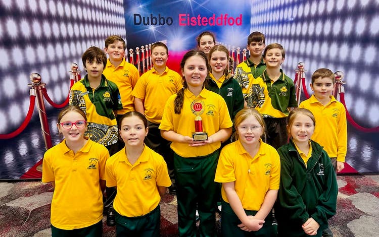 A picture of a group of students in front of Dubbo Esiteddfod banner. The student in the middle is holding a trophy