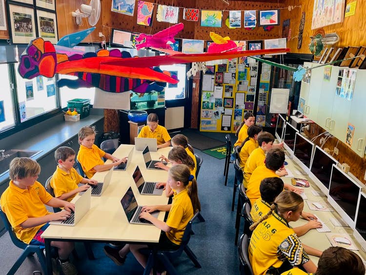 A picture of students sitting in a decorated workspace utilising laptops and desktop computers