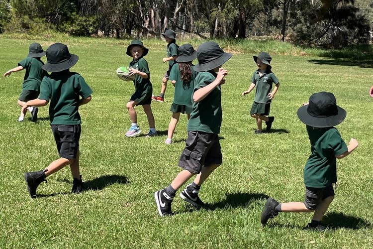 a picture of young students running around on a playing field with a football